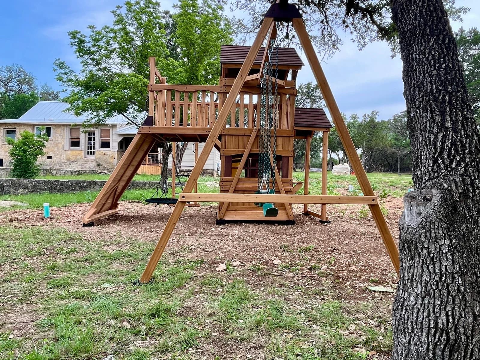 Wooden playset and swing beam in a backyard with mature trees