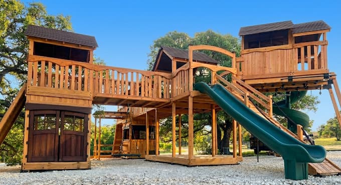A sprawling wooden treehouse playset with bridges and slides in a sunny backyard.